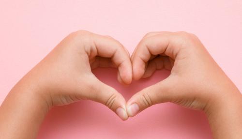 2 hands forming love heart on pink background